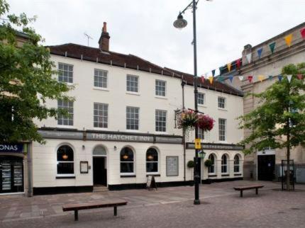 um grande edifício branco com dois bancos à sua frente em The Hatchet Inn Wetherspoon em Newbury