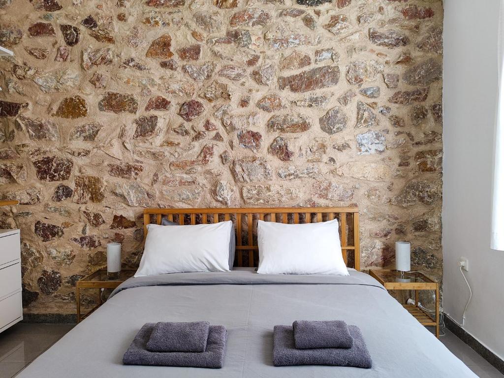 - une chambre avec un mur en pierre et un lit avec 2 serviettes dans l'établissement KYMA Apartments - Athens Acropolis 2, à Athènes