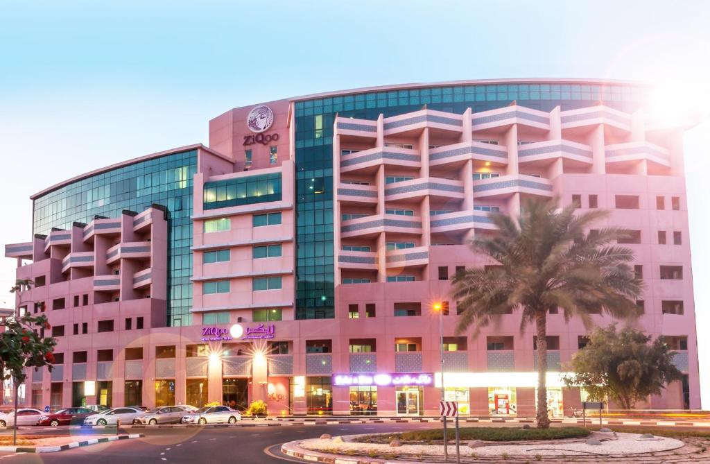 a pink building with a palm tree in front of it at ZiQoo Hotel Apartments Dubai in Dubai