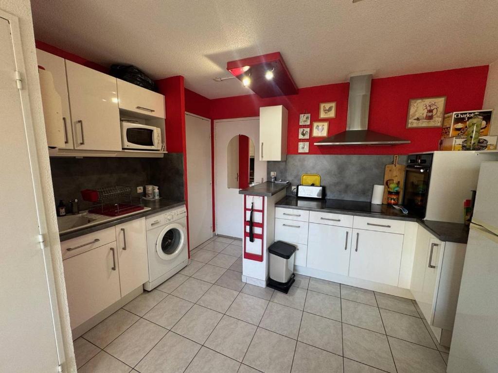 - une cuisine avec des placards blancs et des murs rouges dans l'établissement T2 au Cap d'Agde avec piscine, parking proche plages - FR-1-749-77, au Cap d'Agde