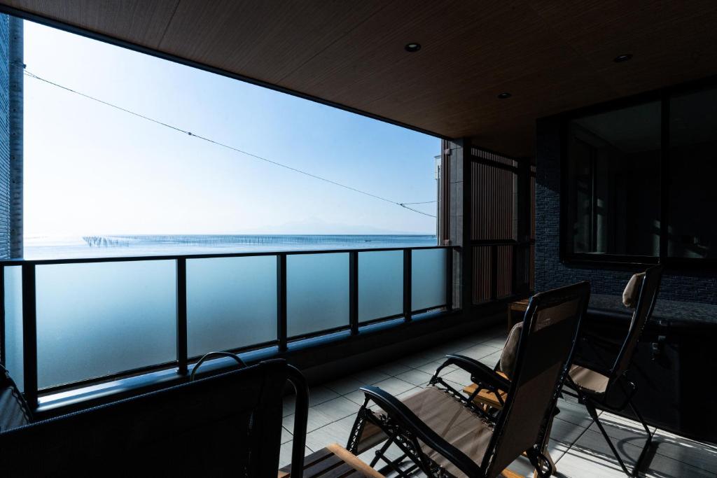 ein Balkon mit Stühlen und Blick auf das Meer in der Unterkunft みらいステイKawachi in Kumamoto