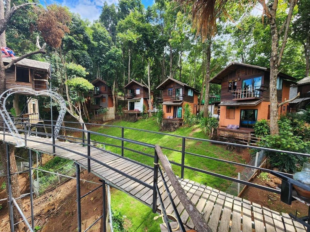 a bridge over a river in a forest with houses at บ้านต้นไม้แม่กำปอง Baan TONMAI MAEKAMPONG in Chiang Mai