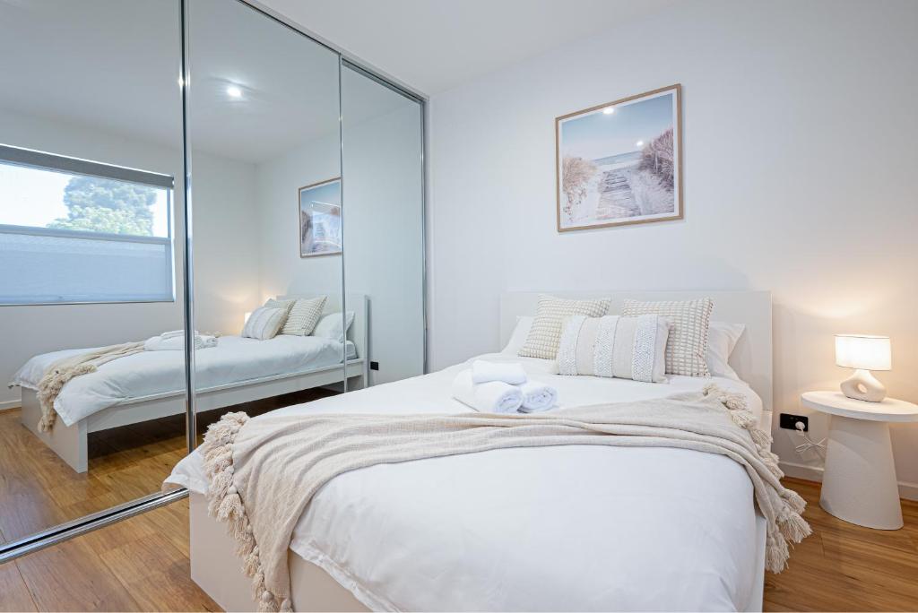 een witte slaapkamer met een bed en een spiegel bij Chic Flinders Park Getaway in Adelaide