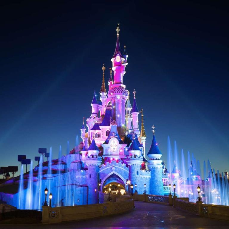 un château de disney est allumé la nuit dans l'établissement Rêve By Dream Apartments, à Serris