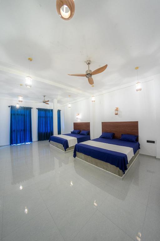 two beds in a white room with blue curtains at Bluesafiya lodge in Matara