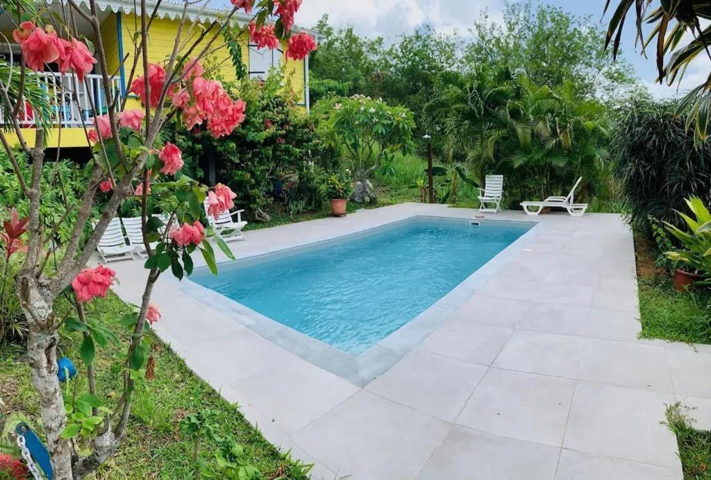 a swimming pool in the backyard of a house with pink flowers at Maison confortable Le Diamant 40 m² avec piscine in Le Diamant