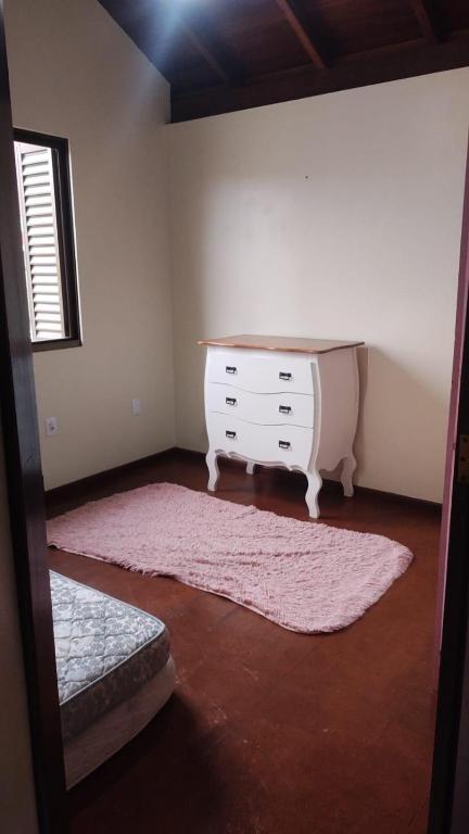 a bedroom with a dresser and a pink rug at Quarto da Tati in Garopaba