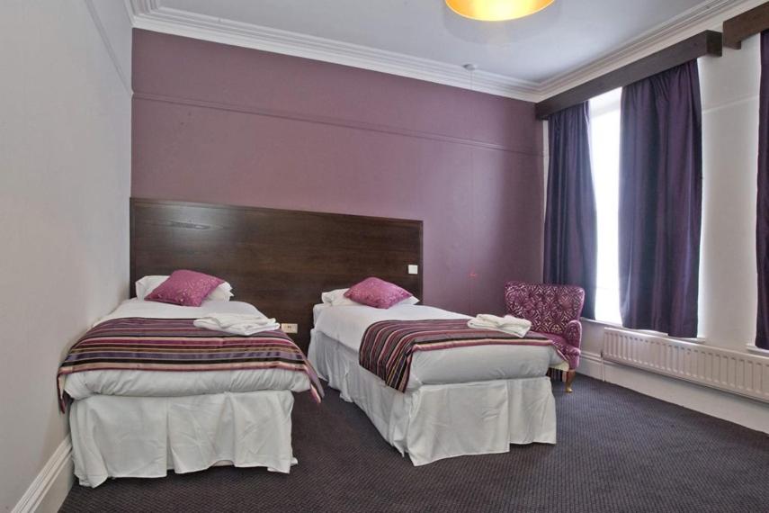 two beds in a hotel room with purple walls at The Duke of Wellington Wetherspoon in Minehead