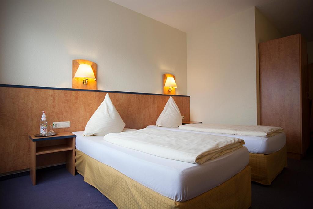 two beds in a hotel room with two lamps on the wall at Hotel Haus Union in Oberhausen