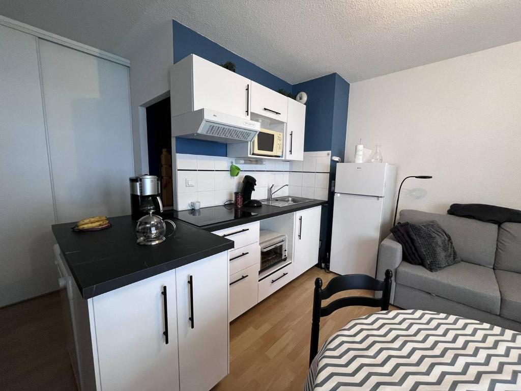 une petite cuisine avec des placards blancs et un comptoir noir dans l'établissement Appartement cosy à Cauterets avec terrasse et local à ski - FR-1-812-84, à Cauterets