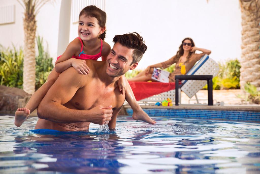 a man holding a child on his back in a swimming pool at Yas Island Rotana Abu Dhabi in Abu Dhabi