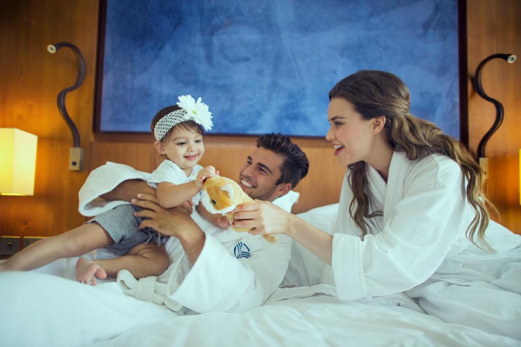 a man and woman sitting on a bed with a baby at Yas Island Rotana Abu Dhabi in Abu Dhabi