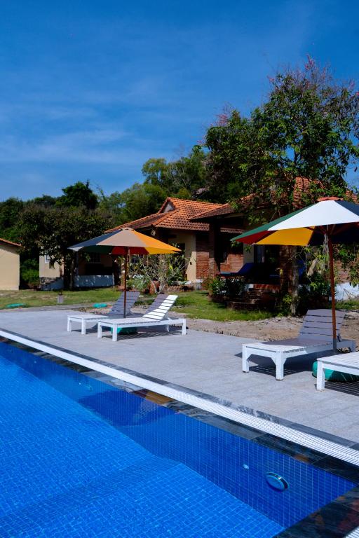 a swimming pool with two umbrellas and two tables at Vung Bau Resort in Phú Quốc