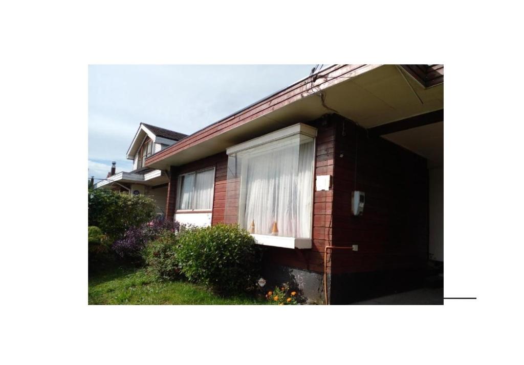 Cette maison en briques rouges est dotée d'une fenêtre avec des rideaux blancs. dans l'établissement Acogedora casa en el sur de Chile, ubicada en barrio residencial, à Puerto Montt