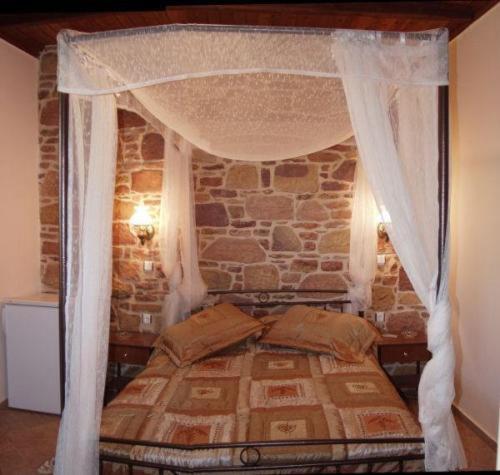 1 dormitorio con cama con dosel y pared de piedra en Manganos Apartments, en Kambos