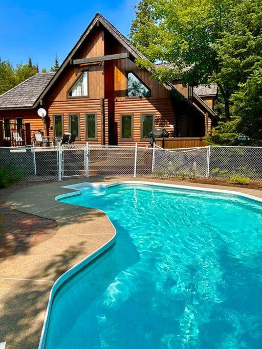 a large blue swimming pool in front of a house at L'Eden - Air climatisé -Golf -Piscine juin à sept - SPA -Billard in Saint-Faustin