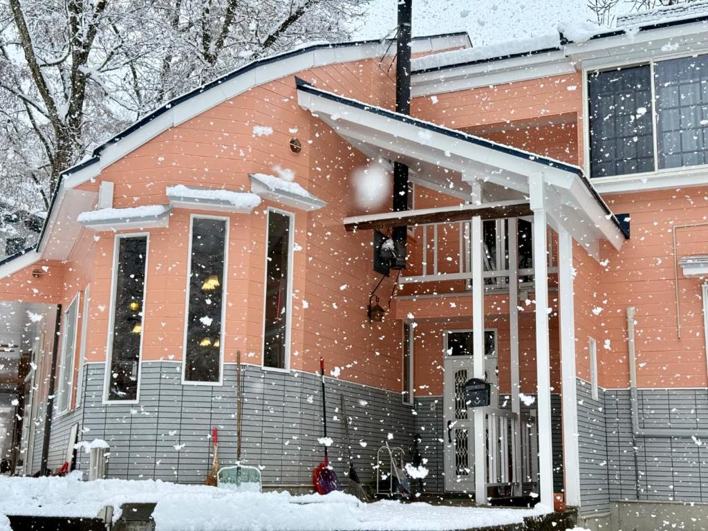 a house covered in snow in front of a house at Hotel Junior Mint Hakuba in Hakuba