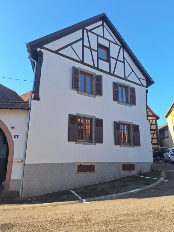 une maison blanche avec des fenêtres à volets noirs dans l'établissement Gîte Les Pivoines, à Dambach-la-Ville