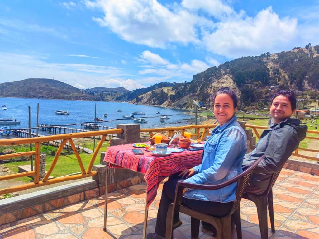 two men sitting at a table on a balcony with a view of the water at Willka Uta in Comunidad Challapampa