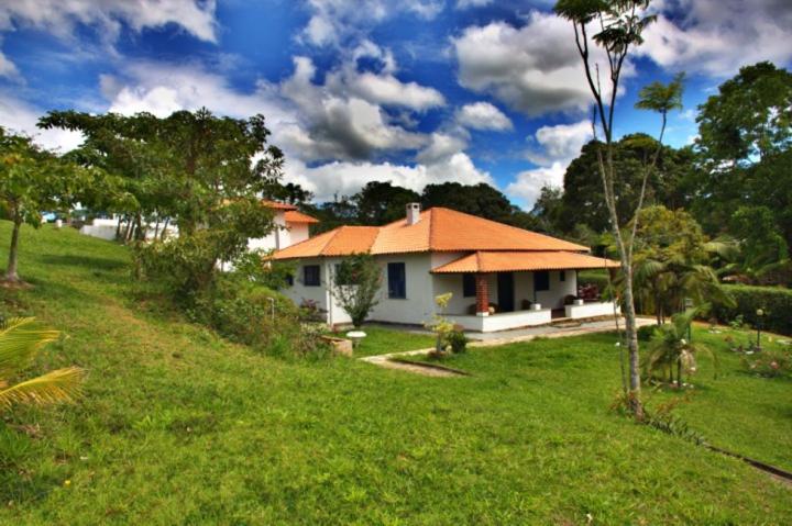 una pequeña casa blanca con techo naranja en un campo en Pousada Coração Verde, en Miguel Pereira