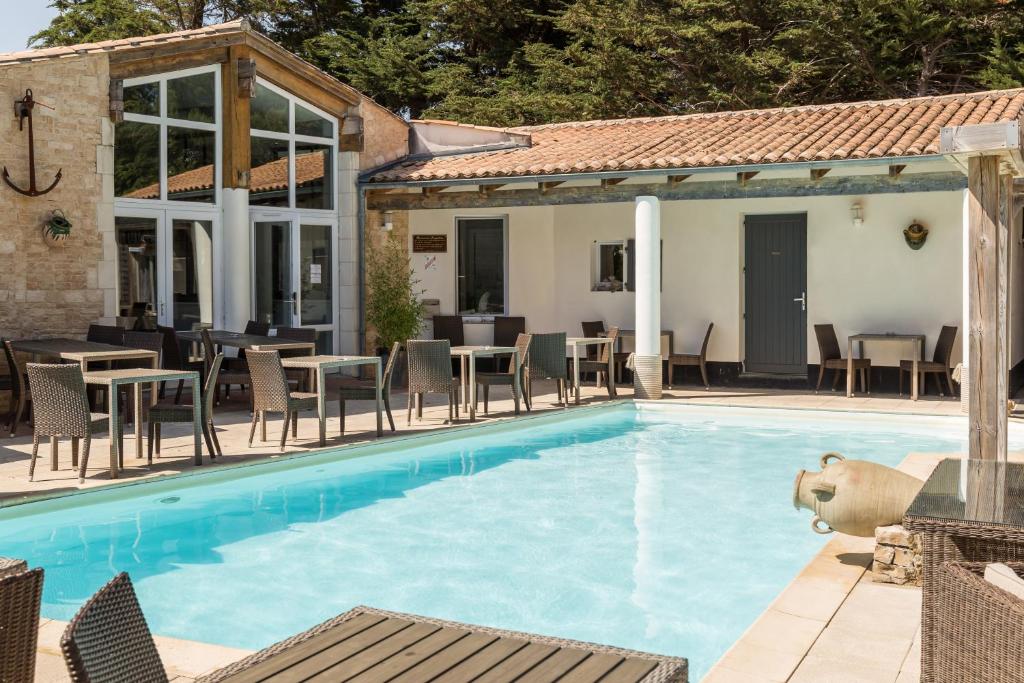 a pool with chairs and tables and a house at Hôtel Restaurant & Spa Plaisir in Le Bois-Plage-en-Ré