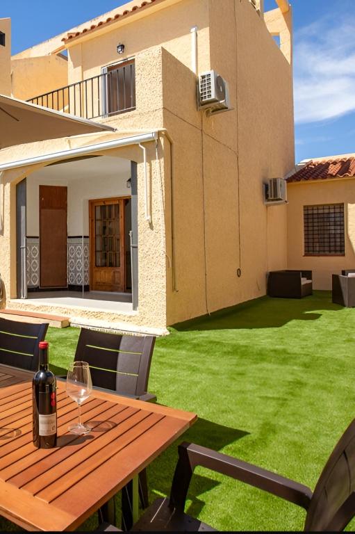 a bottle of wine on a wooden table in front of a house at Bungalow moderno con terraza privada y BBQ a 5 min de la playa in Torrevieja