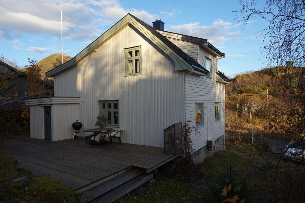 a white house with a wooden deck with a table at Koselig hus ved Kabelvågmarken in Kabelvåg
