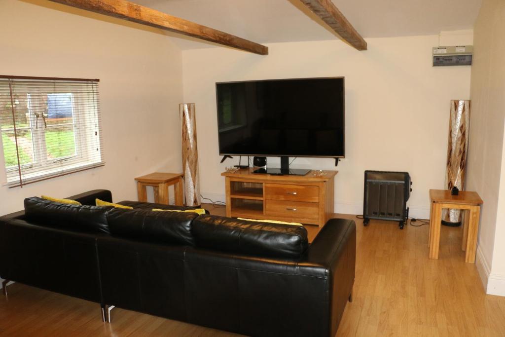 a living room with a black leather couch and a flat screen tv at The Lodge - 2 acres of garden with hot tub and fire pit and BBQ in East Harling