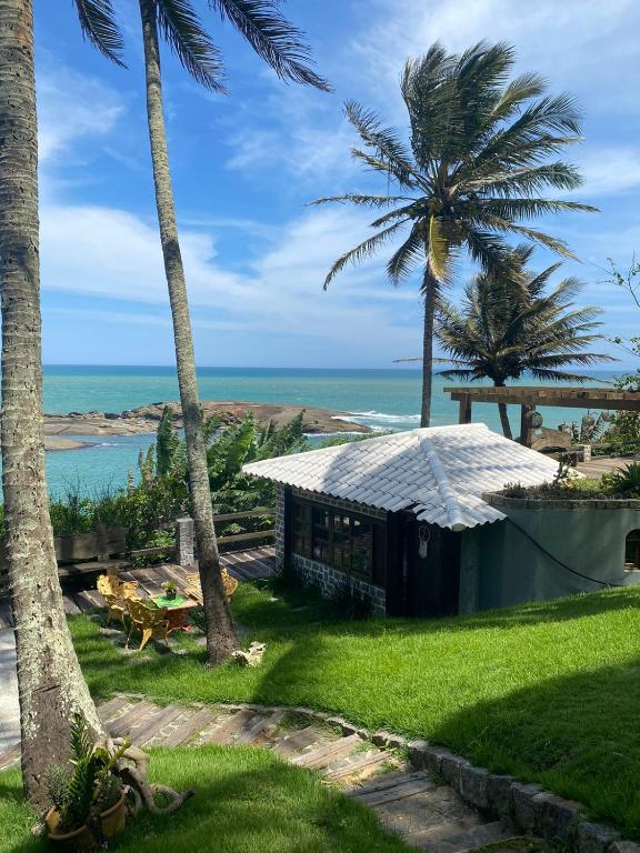 a small building with palm trees and the ocean at Pousada Recanto dos Colibris in Guarapari