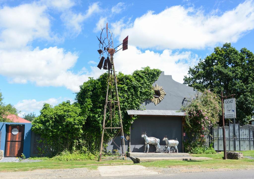 un mulino a vento con due pecore in piedi di fronte a un edificio di The Goat House Cottage a Wakkerstroom