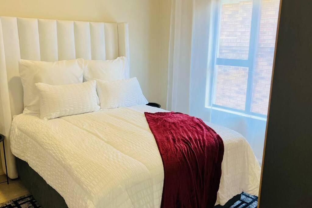 a bed with a red and white blanket and a window at Sunset Haven in Midrand