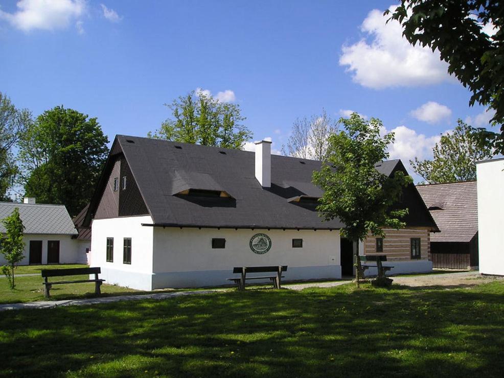 a white building with a black roof with two benches at Penzion Betlém in Hlinsko