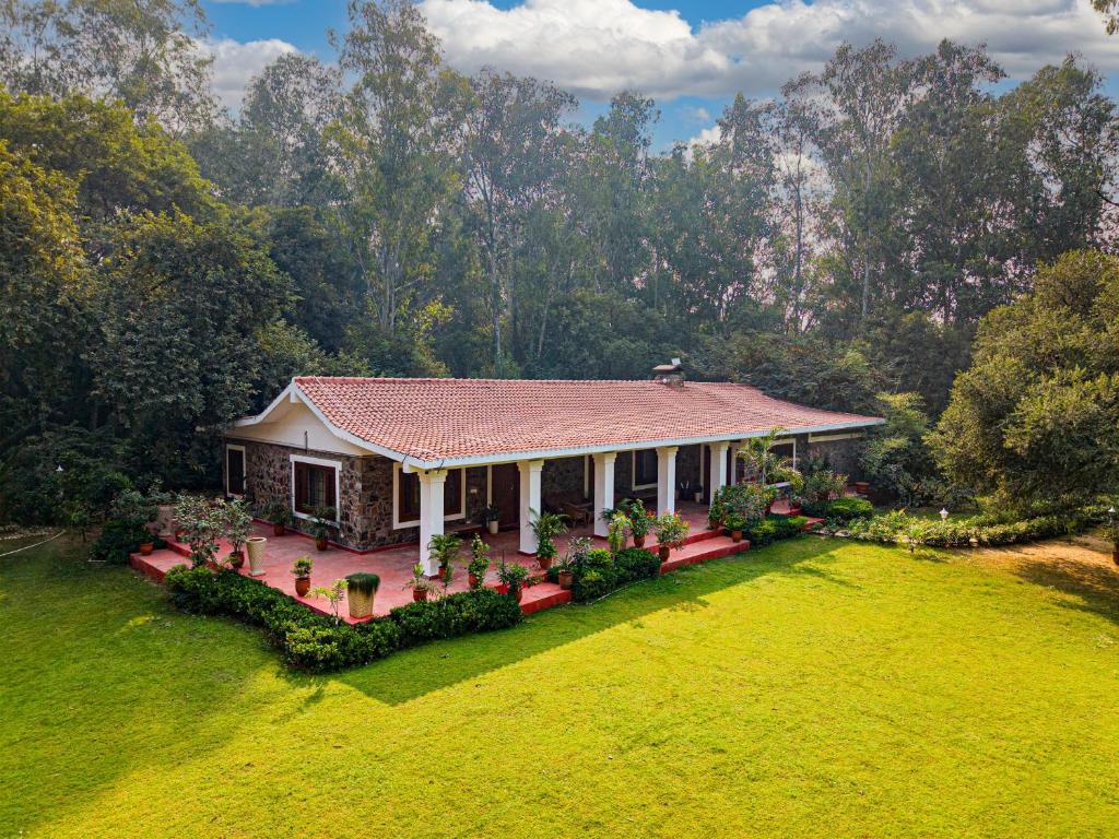 a small house with a red roof on a green field at amã Stays & Trails Bliss Dhauj ,Haryana in Faridabad
