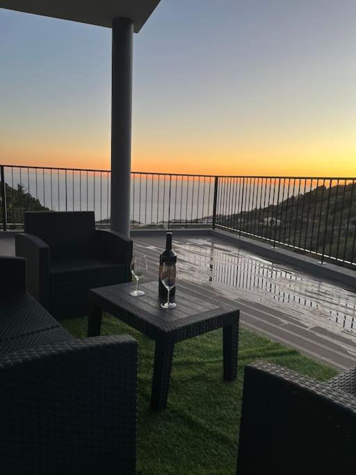 a table with a bottle and glasses on a balcony at Sunset Valley House in Ribeira Brava