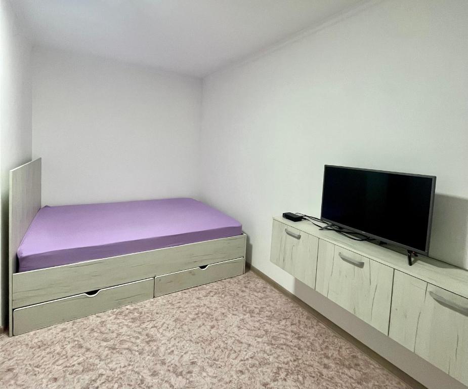 a bedroom with a purple bed and a flat screen tv at Уютная однокомнатная квартира в посёлке Щучинский in Uchitelʼ
