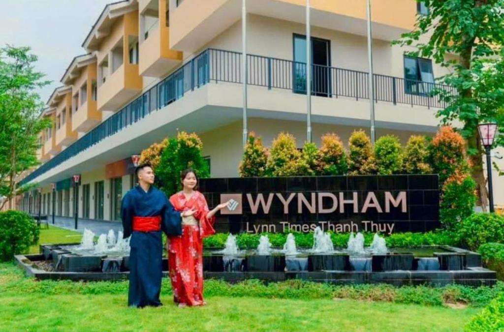 a man and a woman standing in front of a building at Lotus Wyndham Thanh Thủy in Phú Thọ