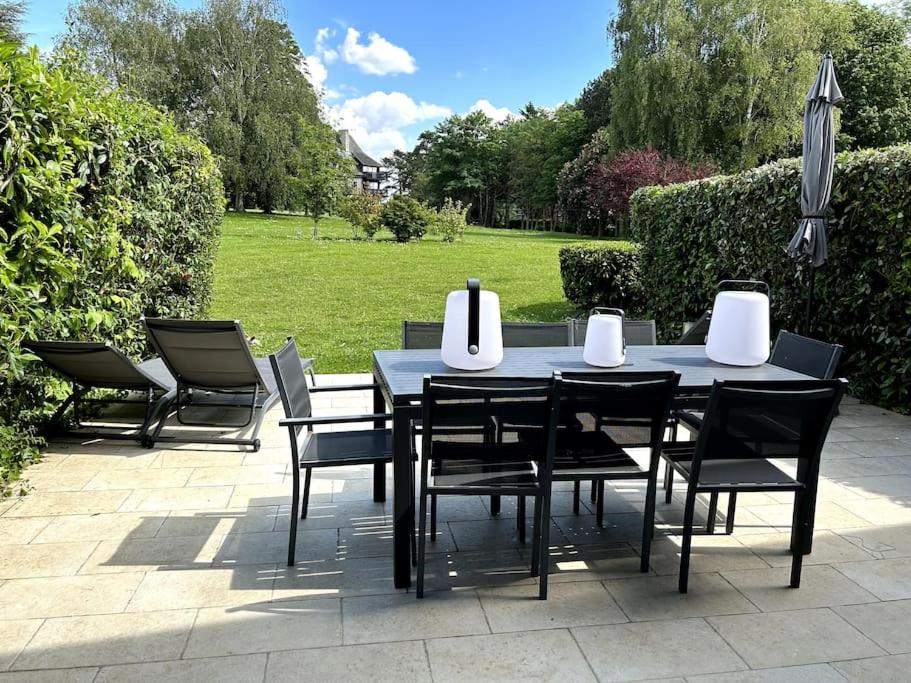 une table à manger et des chaises noires avec un parasol dans l'établissement Manoirs du Golf domaine privé 3 chambres, à Tourgéville
