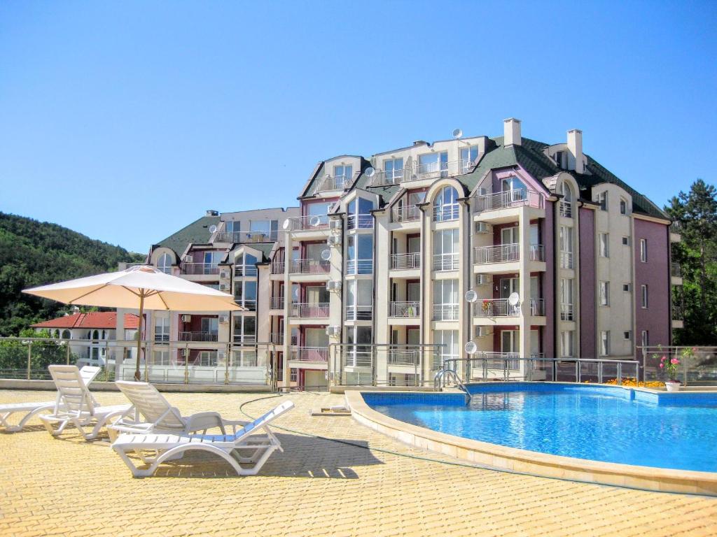 ein großes Gebäude mit einem Pool, Stühlen und einem Sonnenschirm in der Unterkunft Каварна Хилс Апартаменти - Kavarna Hills Apartments in Kawarna