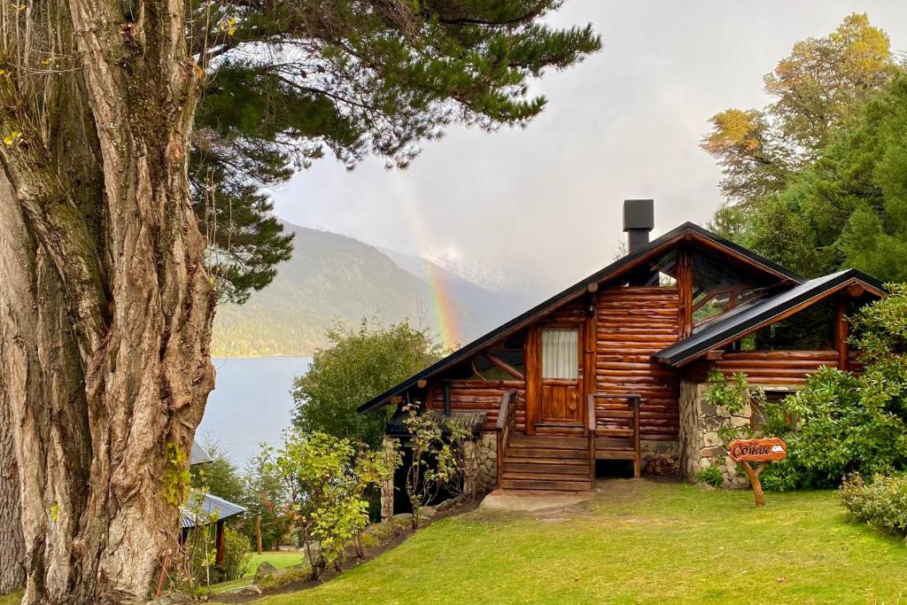 a wooden cabin with a rainbow in the background at Cabañas Villa Labrador con costa de lago in San Carlos de Bariloche