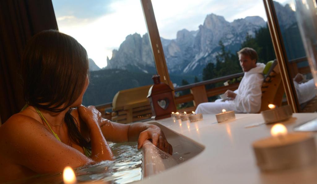 a woman in a hot tub in a room with mountains at Vidor Resort in Pozza di Fassa