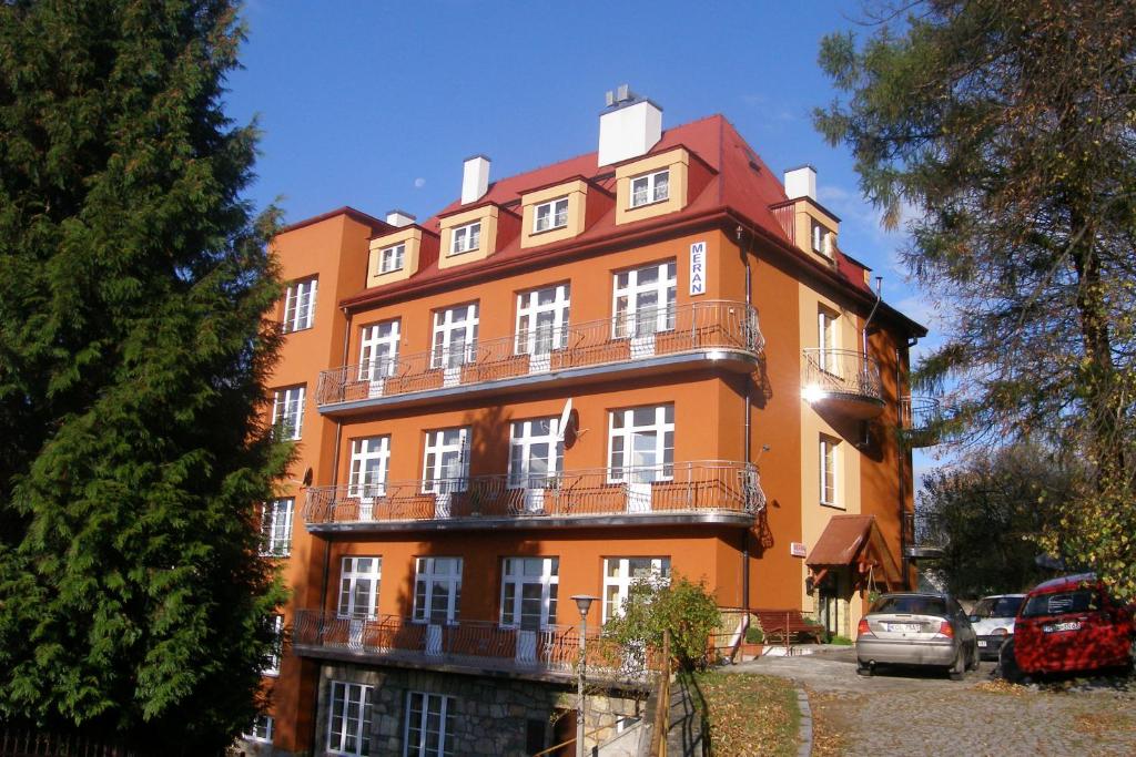pomarańczowy budynek z balkonami i samochodami zaparkowanymi na parkingu w obiekcie Zajazd Meran w mieście Krynica Zdrój