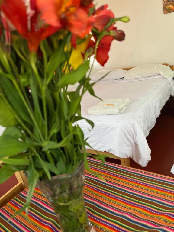 a vase of flowers sitting on a table with a bed at ENEDE HOSTEL in Cusco