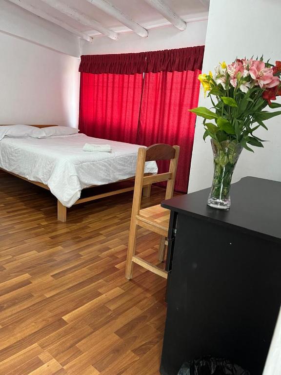 a room with a bed and a table with a vase of flowers at ENEDE HOSTEL in Cusco