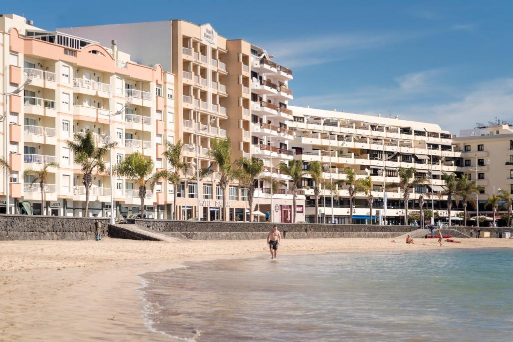 a man standing in the water on a beach with buildings at Checkin Diamar in Arrecife
