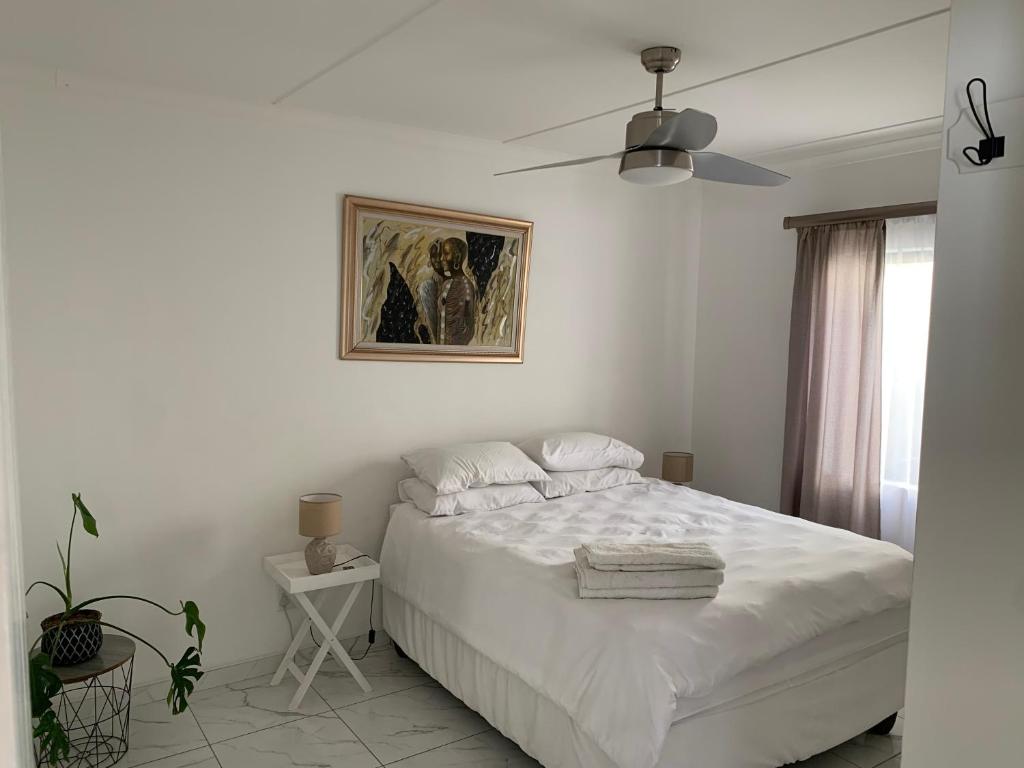 a white bedroom with a bed and a ceiling fan at Luxury 1 Bdr Garden Cottage in Windhoek
