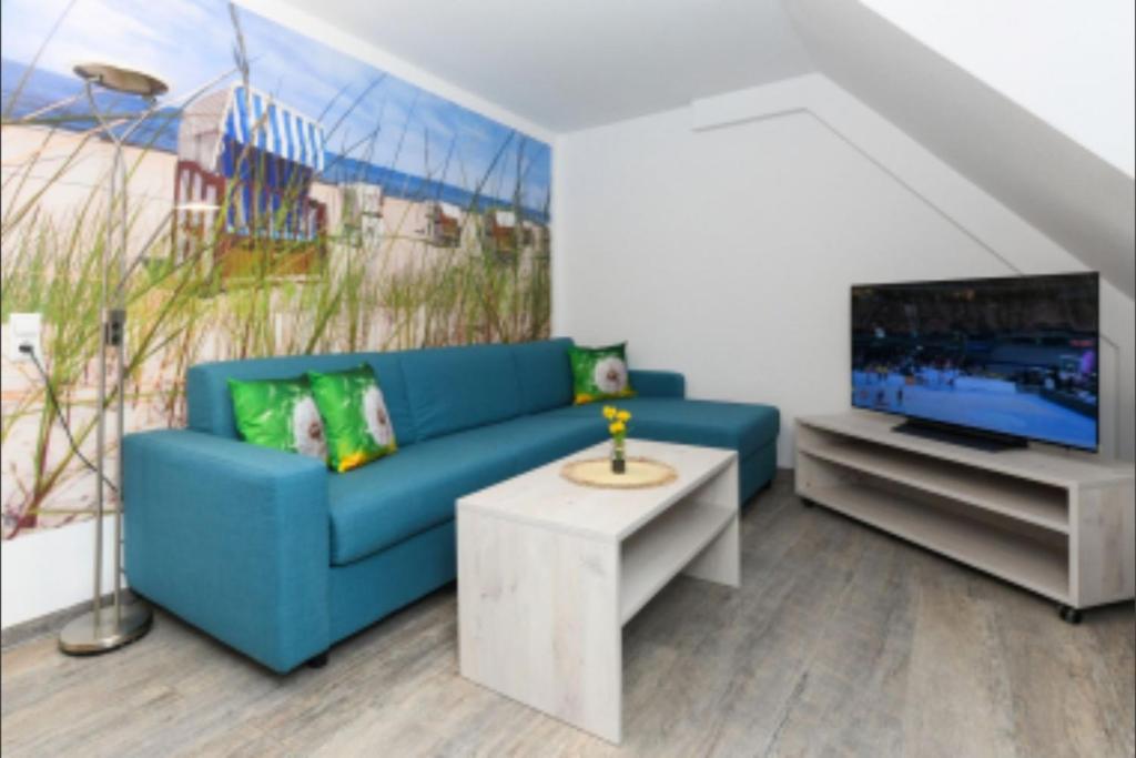 Una sala de estar con un sofá azul y un televisor en Haus Strandkorb FeWo Strandkob 7, en Bensersiel