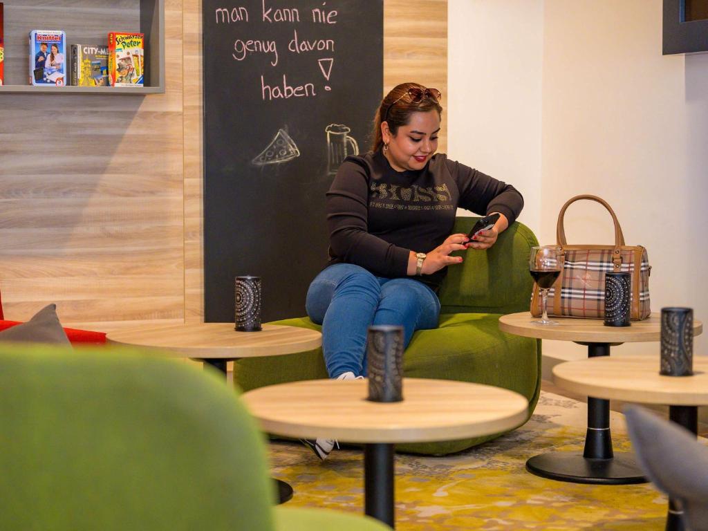 a woman sitting in a chair looking at her cell phone at ibis Stuttgart Airport Messe in Leinfelden-Echterdingen