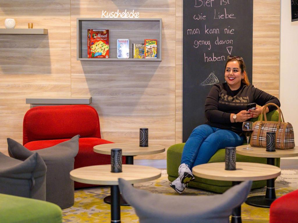 a woman sitting in a chair with a cell phone at ibis Stuttgart Airport Messe in Leinfelden-Echterdingen
