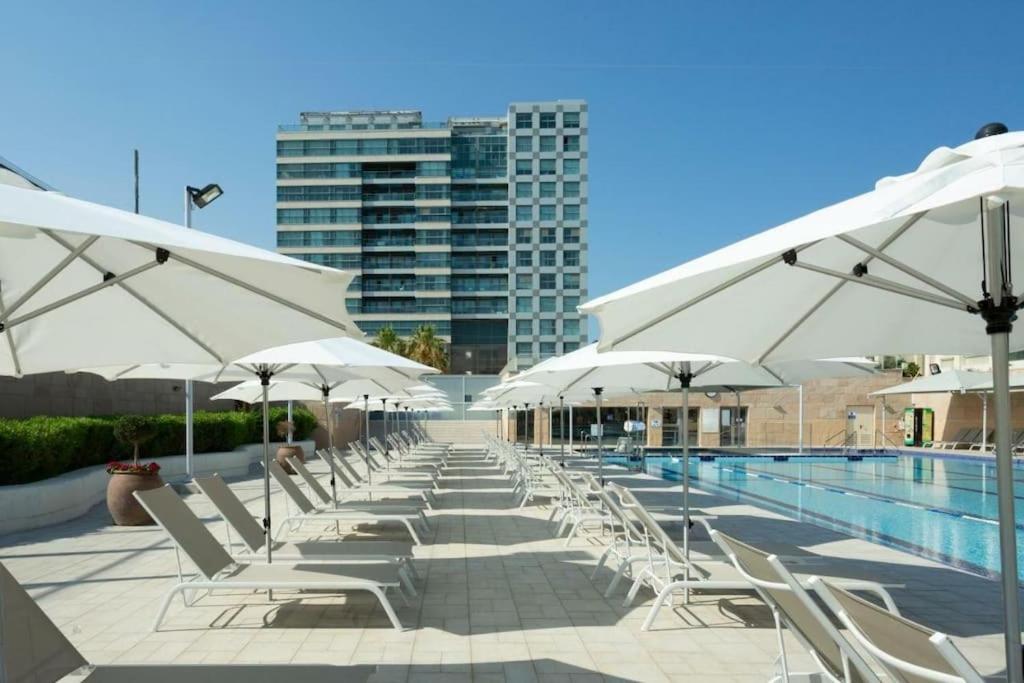 a row of white chairs and umbrellas next to a swimming pool at חדר שינה וסלון ומרפסת נוף לים in Herzliyya B