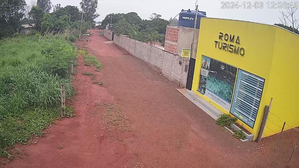 a red dirt road next to a yellow building at Jardim do Éden Hostel e Camping in Estivado